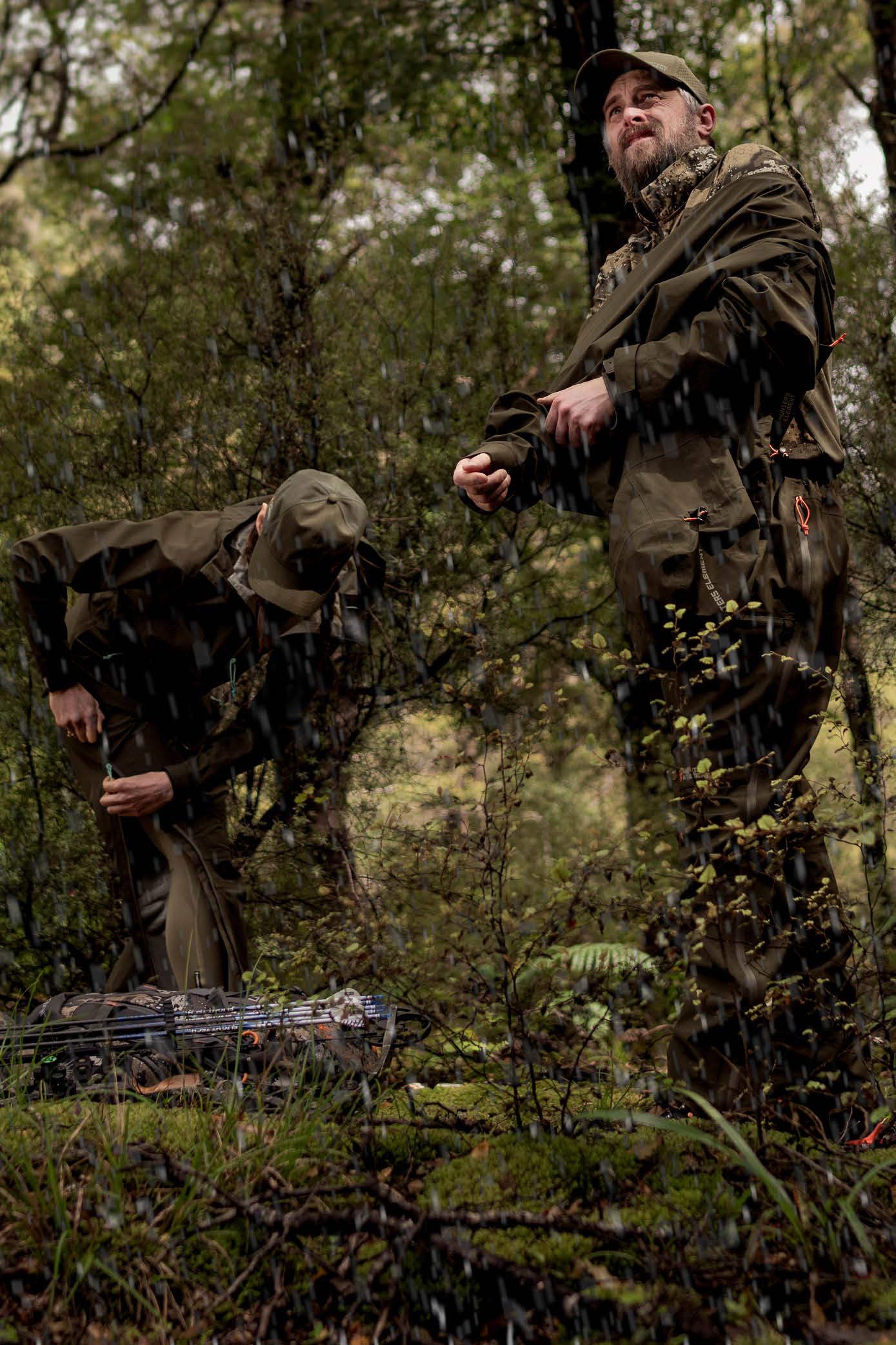 Two hunters in camouflage gear in a forest setting with rifles.