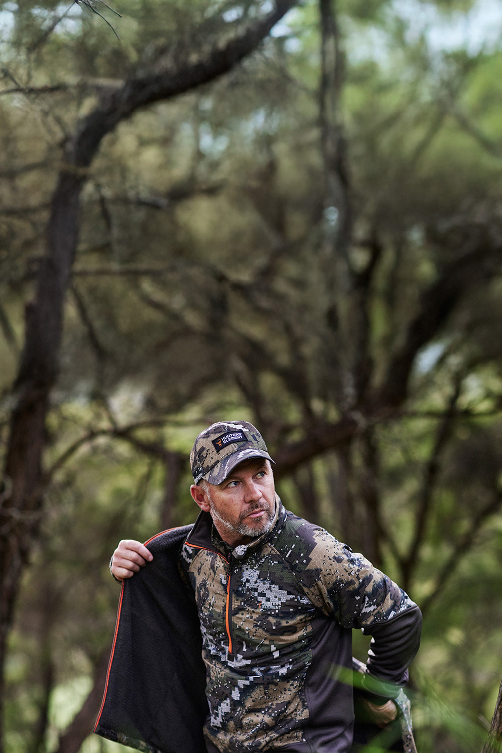 Man in camouflage clothing and cap walking through a forest