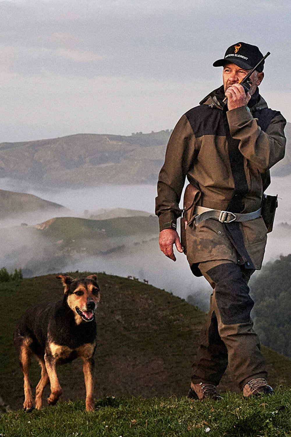 Man in outdoor gear with a dog on a mountainous landscape