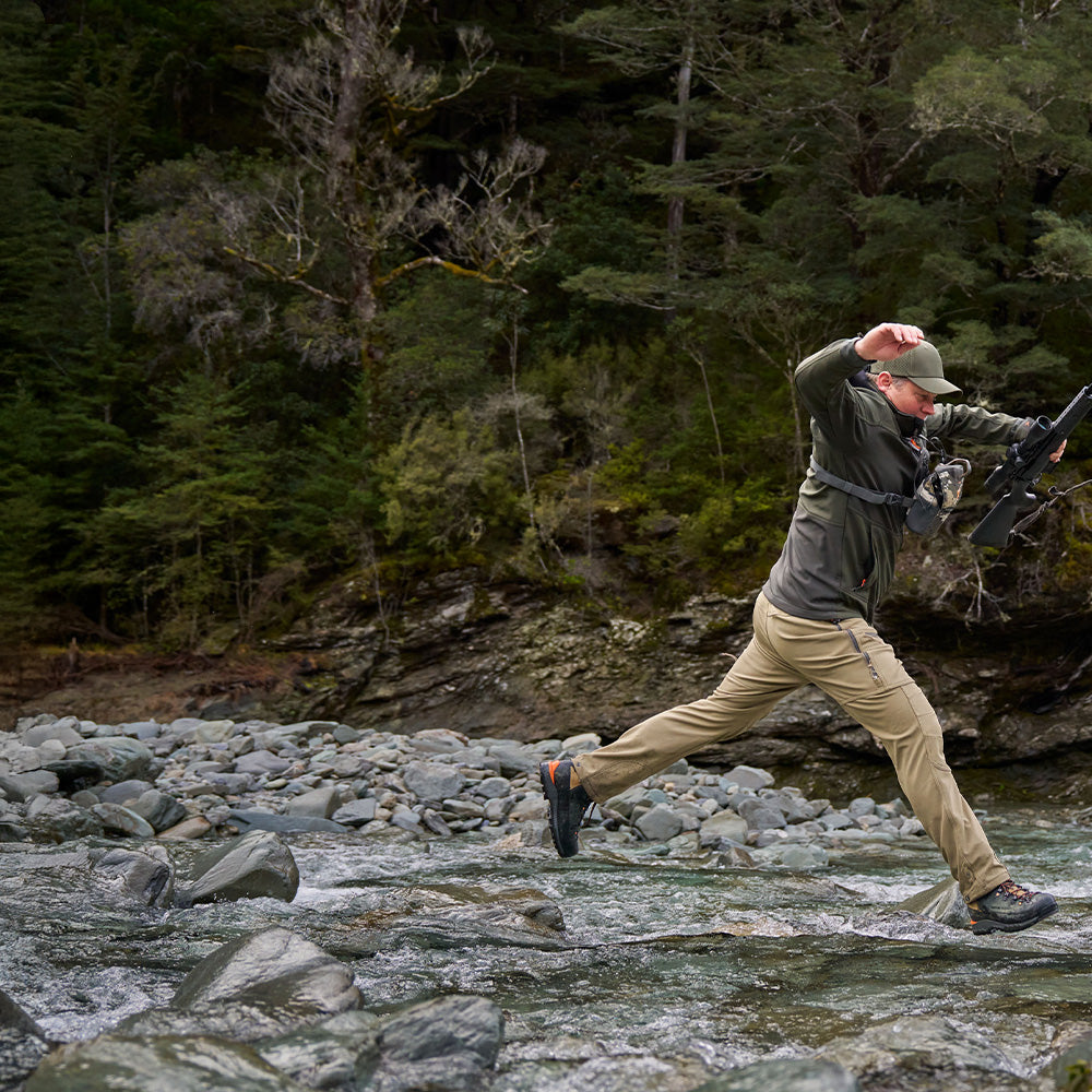 Spur Pants homepage mobile banner showing Cody jumping over a river wearing the Tussock Spur Pants.
